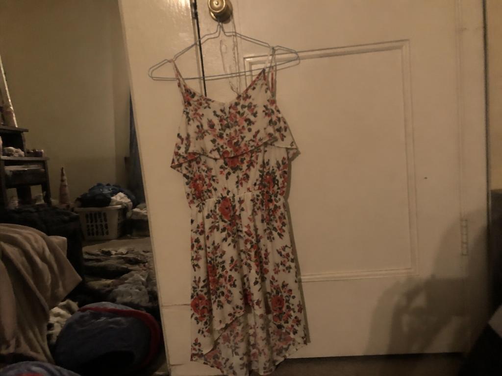A floral dress on a wire hanger against a bedroom door in yellow light