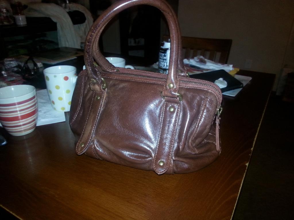 A brown leather handbag on a cluttered dining table in dim evening light