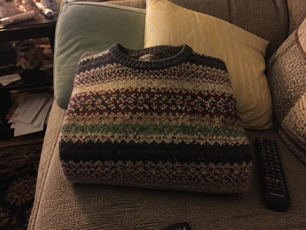 A patterned knitted jumper folded on a messy sofa in dim lamp light